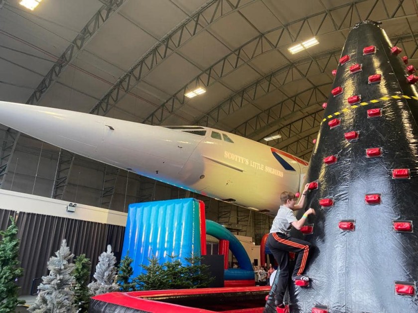 A large plane in a hangar at the Scotty's 2021 Christmas party, alongside a Scotty member climbing an inflatable wall