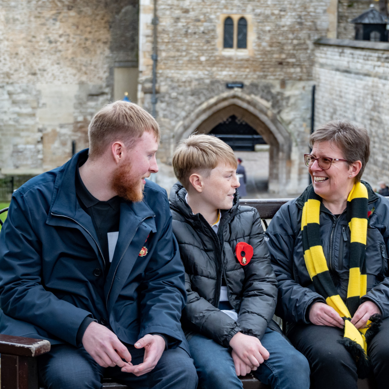 Scotty's Little Soldiers bereavement specialist wearing yellow & black scarf, with two bereaved young people, wearing a Remembrance poppy, at the Tower of London