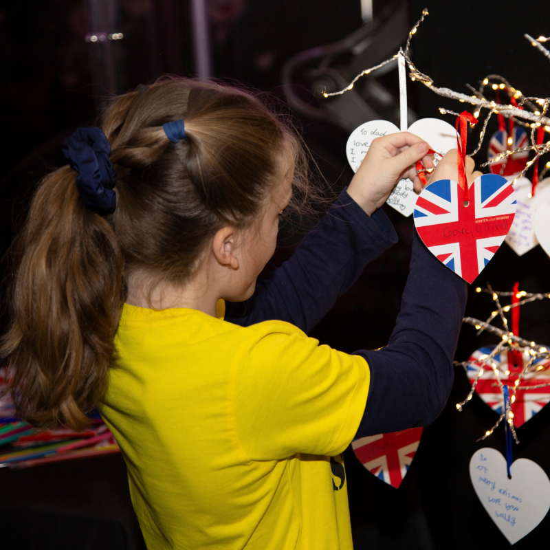 Grieving child at Scotty's Little Soldiers Christmas Party hangs a message to her parent on the Memory Tree